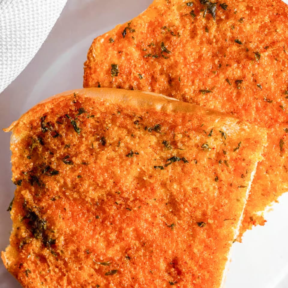 Close-up of two pieces of golden-brown garlic bread with green herbs on a white plate.