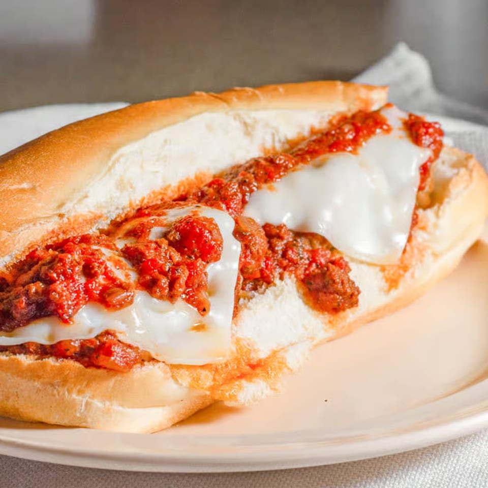 A Marco Polo Pizza meatball sub with marinara sauce and melted mozzarella cheese on a plate.