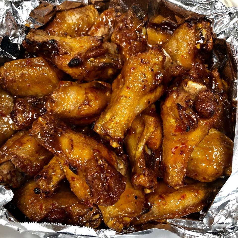 Marco Polo Pizza's sticky, glazed chicken wings with a hint of spice, served in a foil container.