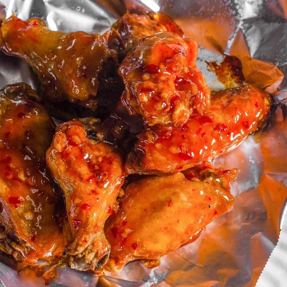 Sweet chili chicken wings from Marco Polo Pizza, glistening with sauce in a foil container.