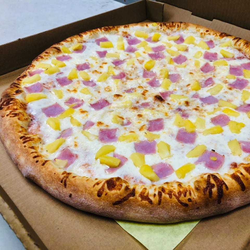 A Marco Polo Pizza Hawaiian pizza with ham and pineapple in a cardboard box.