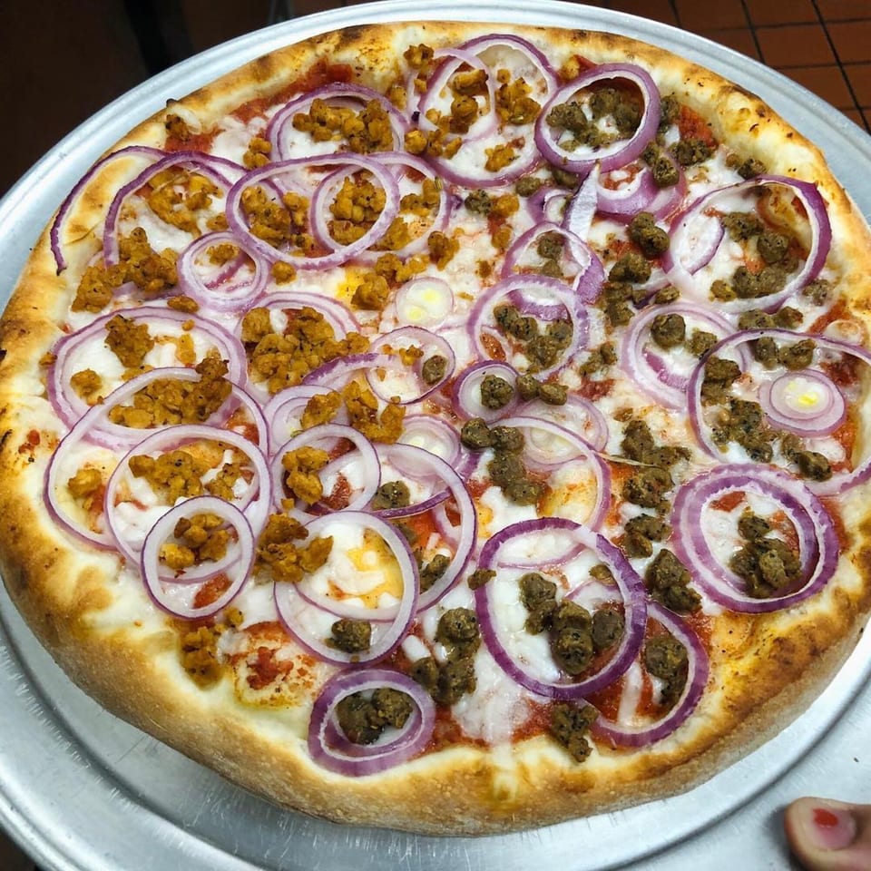 Marco Polo Pizza with red onions, and two types of crumbled sausage on a metal tray.