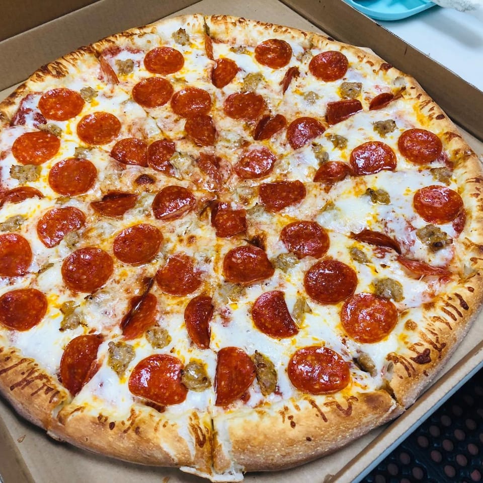 A whole Marco Polo Pizza with pepperoni and sausage in a cardboard box.